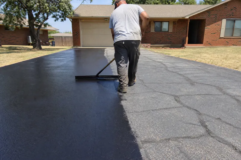 Worker squeegeeing fresh black sealcoat onto an oxidized gray asphalt driveway in Oklahoma summer sun