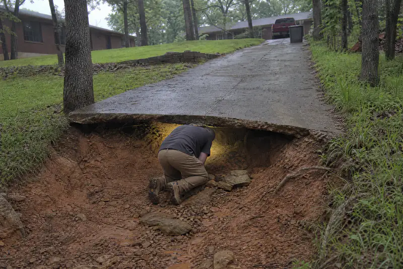 Runoff-carved void under the edge of a sloped concrete driveway on a hillside lot north of Oklahoma City